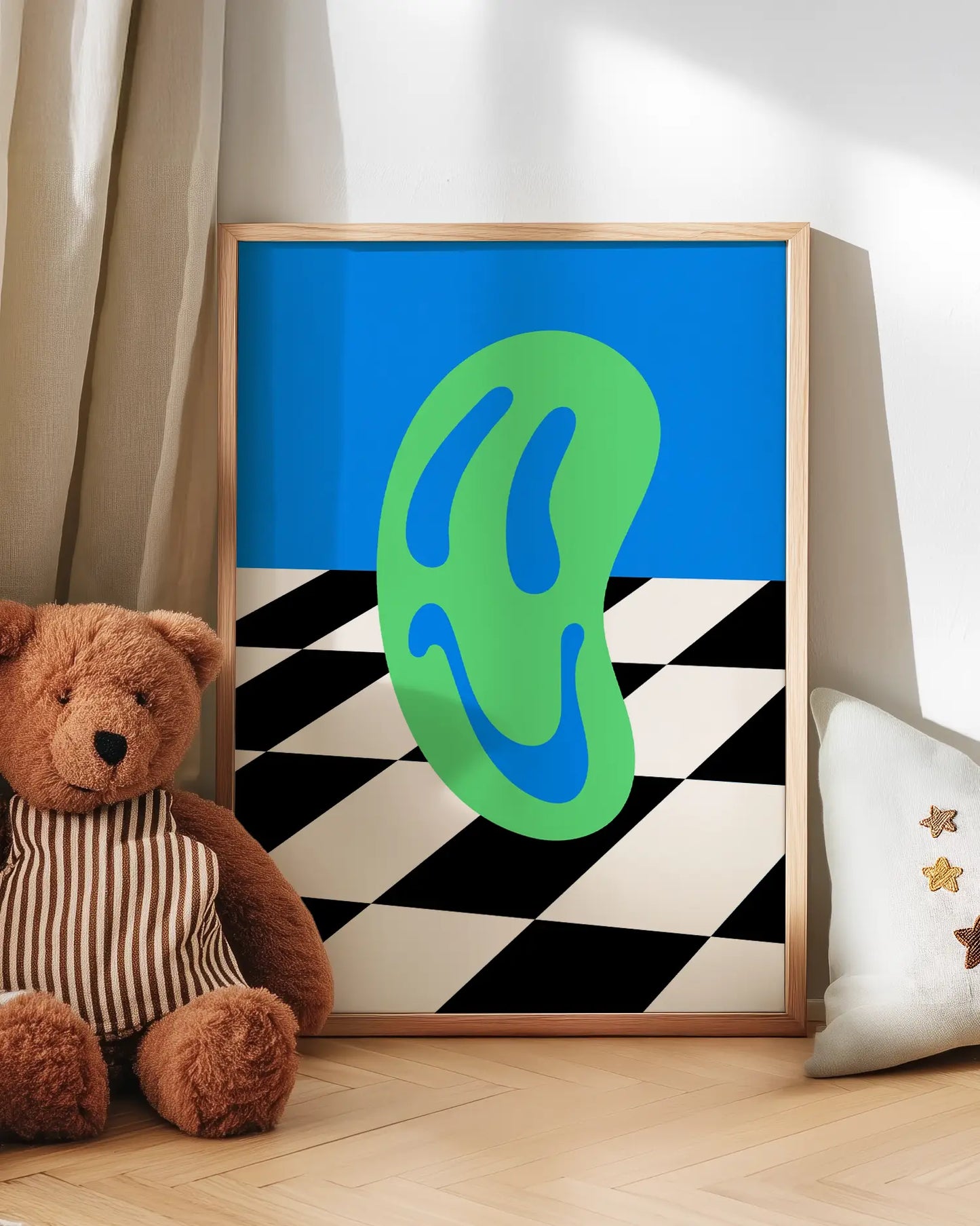 Wall art with a green smiley on a blue and checkered background, next to a teddy bear and a pillow.