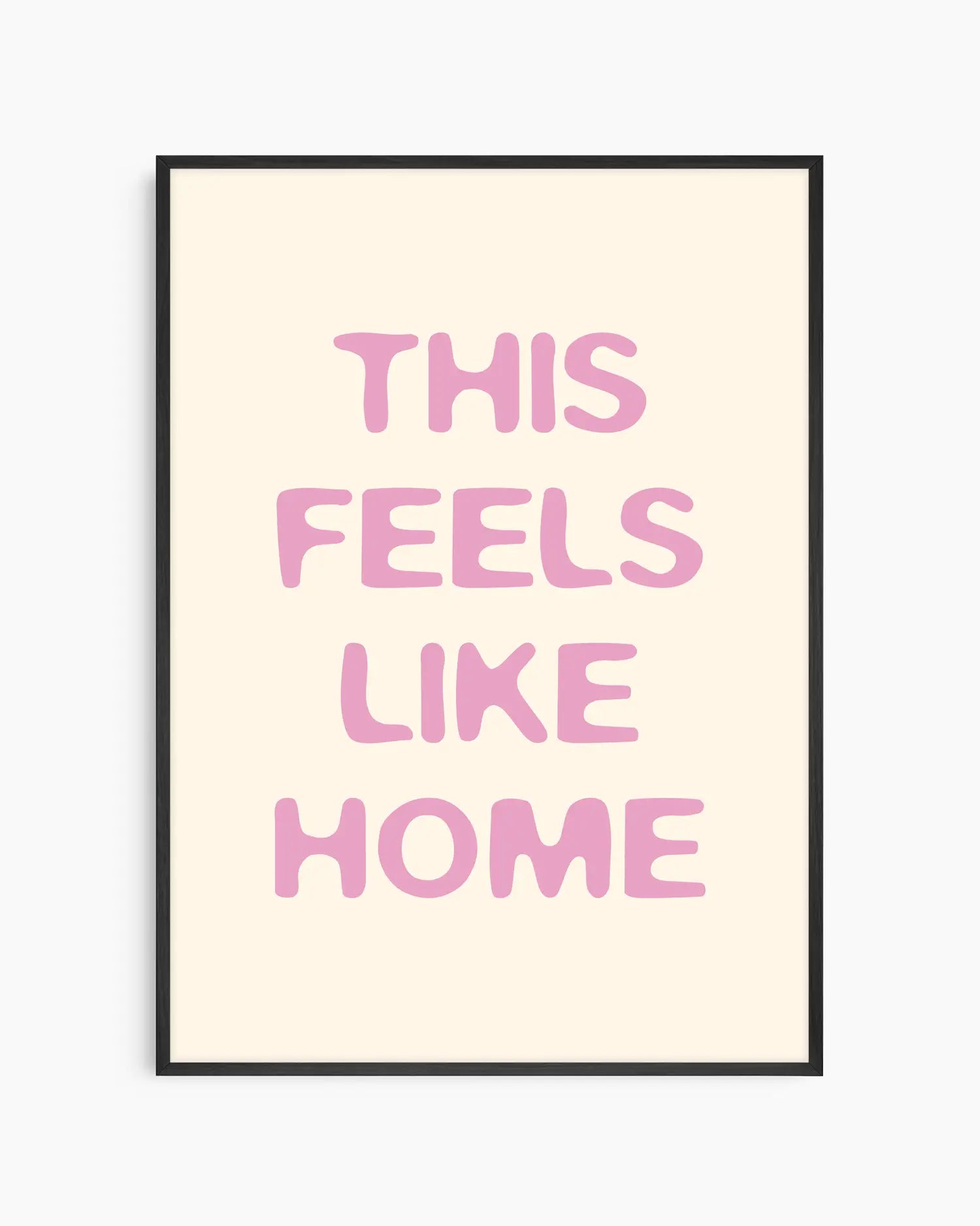 Nursery poster with the text 'This feels like home' written in pink on a beige background, framed in a black wooden frame