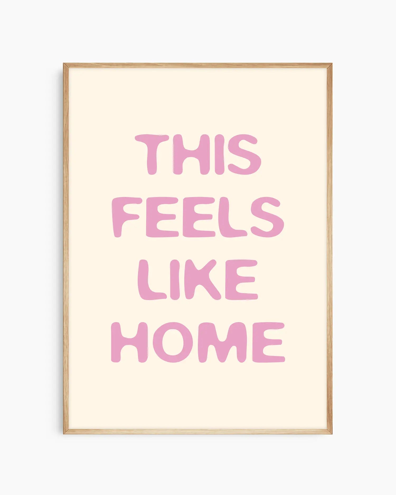 Nursery poster with the text 'This feels like home' written in pink on a beige background, framed in an oak frame