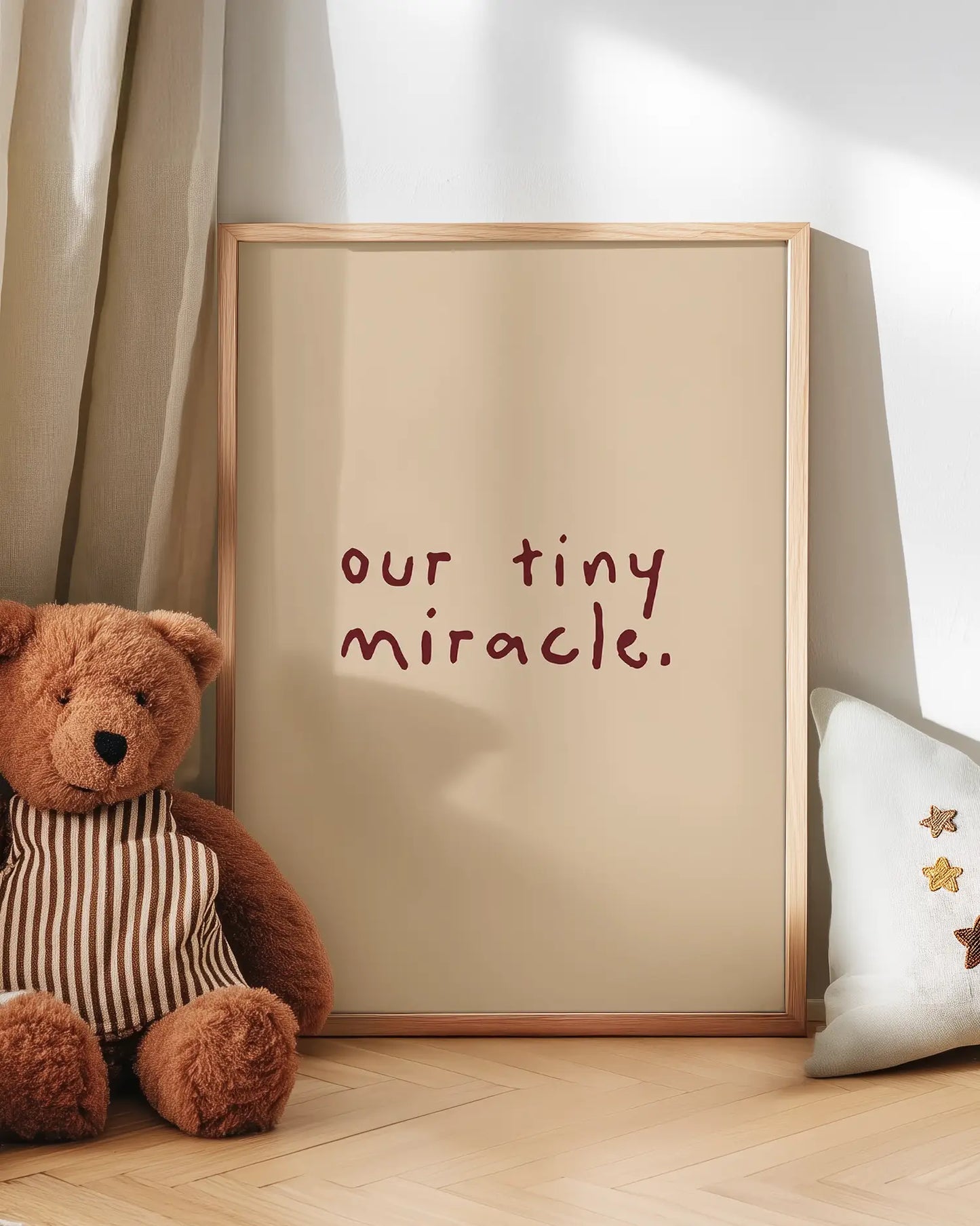 Teddy bear next to a framed poster with 'our tiny miracle.' text on a wooden floor.