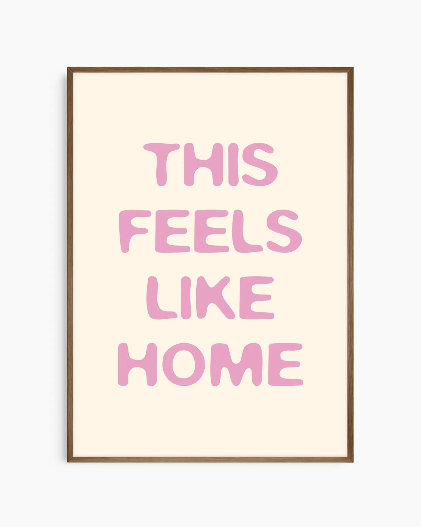 Nursery poster with the text 'This feels like home' written in pink on a beige background, framed in a dark oak frame