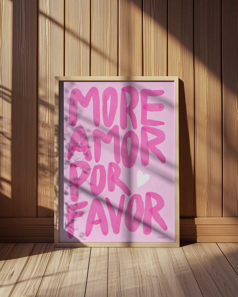 Framed nursery poster with pink text 'MORE AMOR POR FAVOR' leaning against a wooden wall.