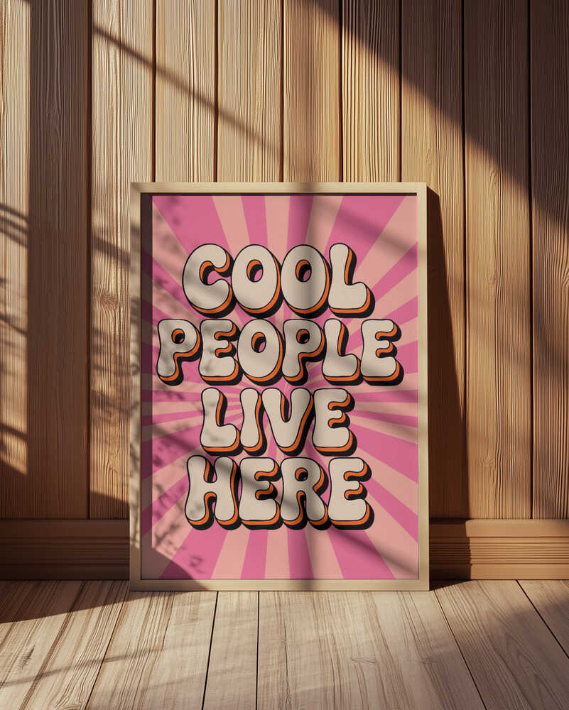Pink poster in 70's style with the text 'Cool people live here' written on it. Leaning against a wooden wall.